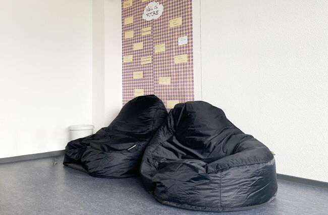 Zwei bequeme schwarze Sitzsäcke stehen in einem modernen Aufenthaltsraum neben einer bunten Wand mit Notizen.
