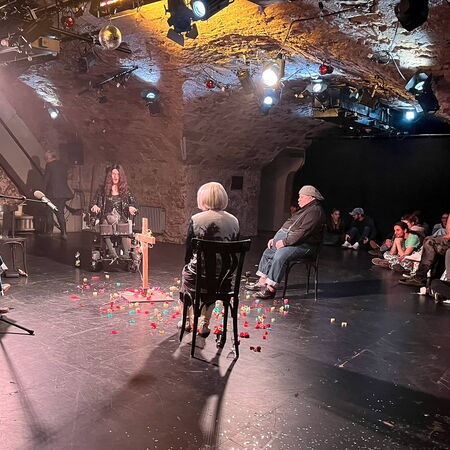 Ein intimes Theaterstück findet in einem stimmungsvoll beleuchteten Gewölbekeller statt, umgeben von aufmerksamem Publikum.
