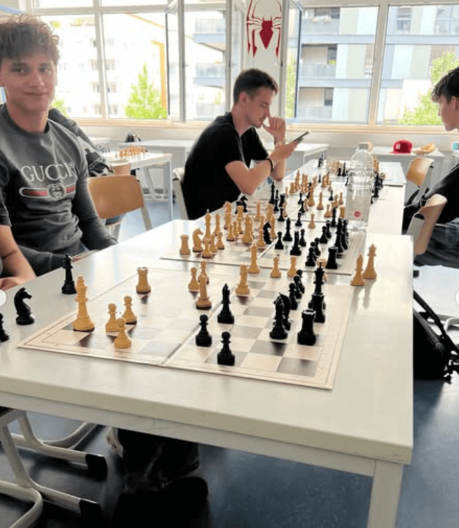Drei Schüler spielen konzentriert Schach in einem hellen Klassenraum während des Projekttags.