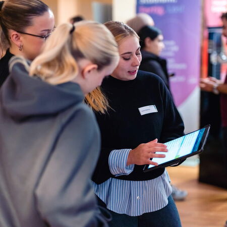Eine Frau zeigt zwei anderen Personen auf einem Tablet Informationen bei einem Networking-Event.