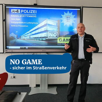 Ein Polizist hält einen Vortrag über Verkehrssicherheit vor einer Präsentation mit dem Titel "No Game".
