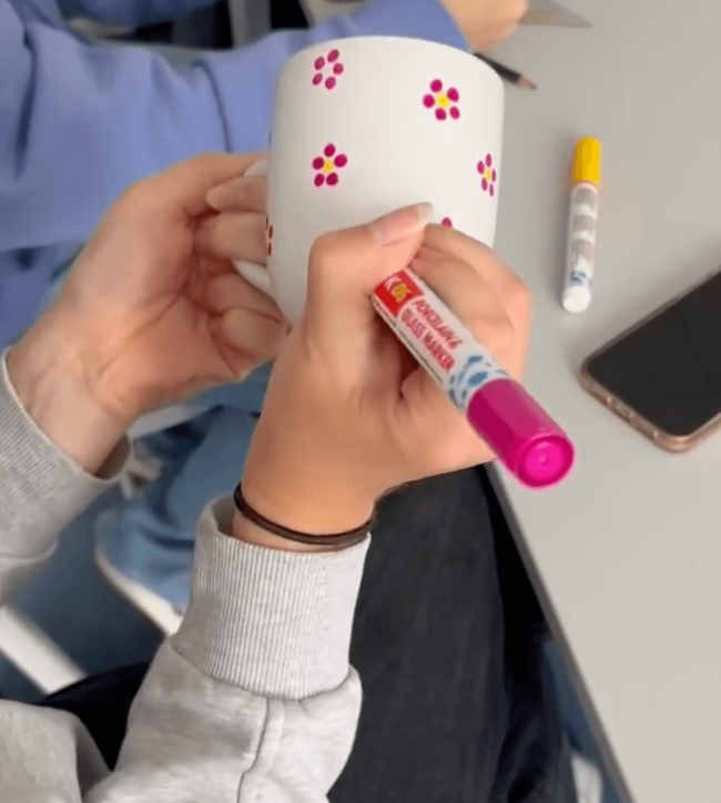 Ein Schüler gestaltet eine weiße Tasse mit bunten Blumenmotiven und einem Markierungsstift während eines Projekttags.