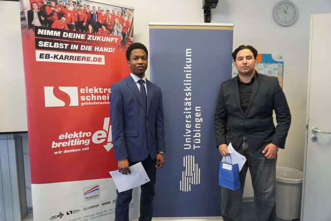 Zwei Männer in Anzügen stehen vor Bannern der Universitätsklinik Tübingen und EB-Karriere bei einer Veranstaltung.