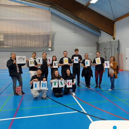 Eine Gruppe hält Plakate mit dem Wort "DIVERSITY" beim IB-Tag in einer Sporthalle. | © IB
