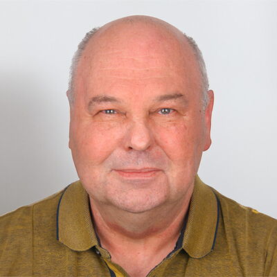 Ein Mann mit Glatze und einem olivgrünen Hemd lächelt sanft in die Kamera vor einem neutralen Hintergrund.