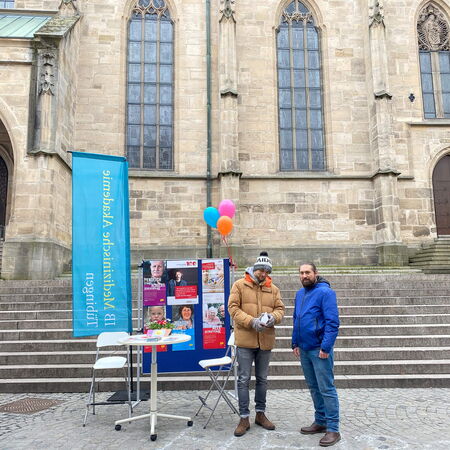 Zwei Männer stehen vor einem Infostand der Logopädieschule am Holzmarkt in Tübingen, mit bunten Luftballons dekoriert.