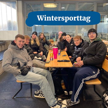 Eine Gruppe junger Menschen sitzt lächelnd an einem Tisch während des Wintersporttags.