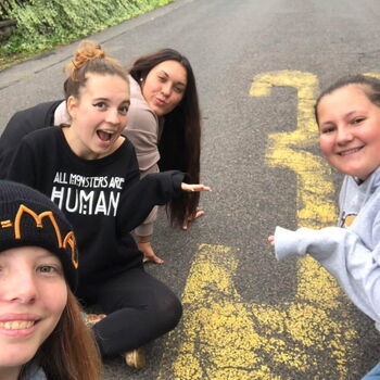 Vier lachende junge Frauen posieren auf einer Straße neben einer gelben Zahl 30 auf dem Asphalt.