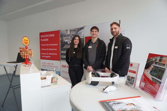 Drei Personen stehen vor einem Messestand mit Informationsmaterial und einem Lollipop-Ständer zur Präsentation von Haustechnik.