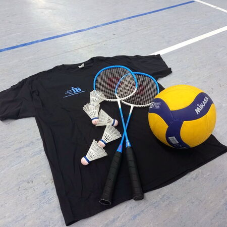 Ein schwarzes T-Shirt liegt auf dem Boden neben zwei Badmintonschlägern, Federbällen und einem gelben Volleyball.