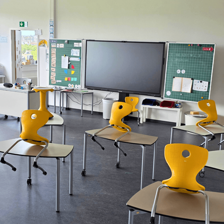 Ein Klassenzimmer mit gelben Stühlen auf Tischen und interaktiver Tafel in der Grundschule Flugfeld Böblingen.