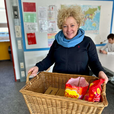 Eine lächelnde Frau trägt einen Korb voller Geschenke zum Zuckerfest in einem Klassenraum.