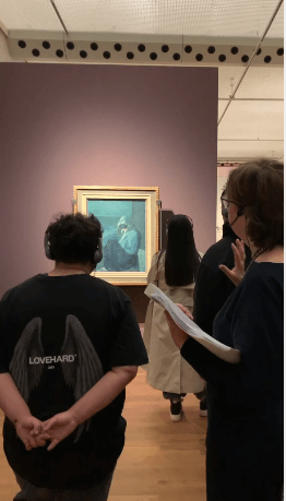 Menschen betrachten ein Gemälde in der Staatsgalerie, während eine Frau mit Notizen darüber spricht.