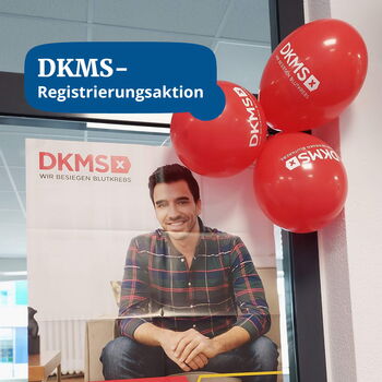 Ein DKMS-Plakat mit einem lächelnden Mann wird von roten Ballons begleitet, die eine Registrierungsaktion ankündigen.