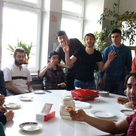 Eine Gruppe von Menschen sitzt um einen Tisch und genießt gemeinsam eine Mahlzeit in einem sonnigen Raum.