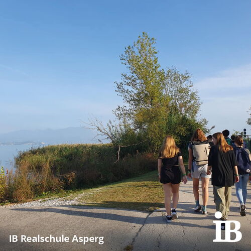 Eine Gruppe von Schülern spaziert bei sonnigem Wetter auf einem Pfad am See entlang während einer Abschlussfahrt.