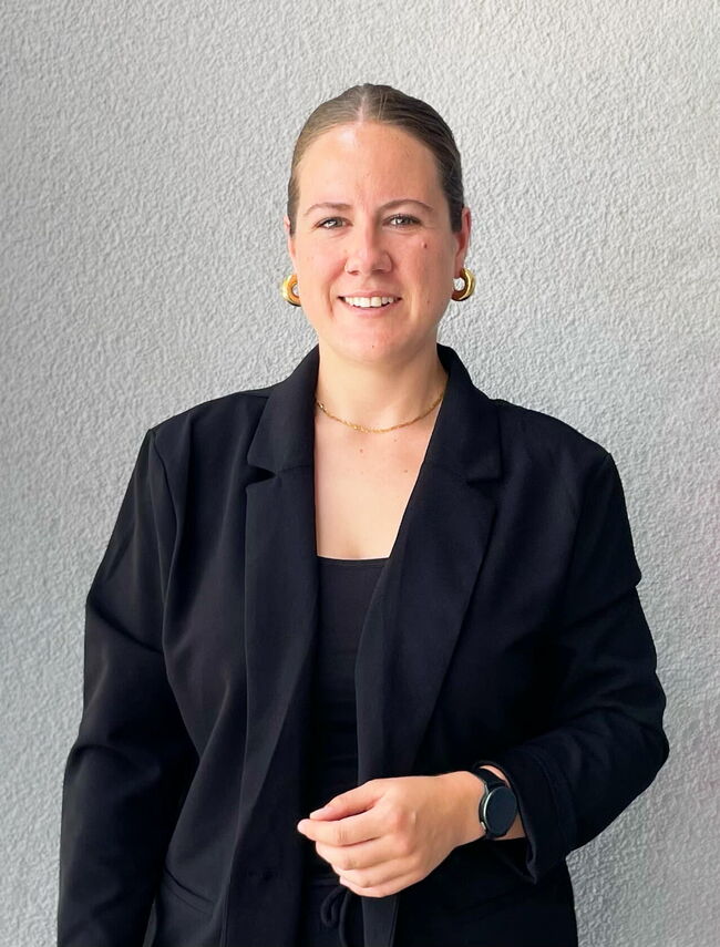 Eine Frau in einem schwarzen Blazer lächelt vor einer hellen Wand an der Grundschule Flugfeld Böblingen.