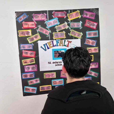 Eine Person betrachtet ein Plakat mit dem Titel "Vielfalt" und vielen bunten Augenbildern. | © Name