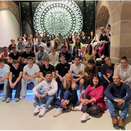 Eine große Gruppe von Menschen posiert vor einem kunstvollen QR-Code-Muster in einem Gebäude in Nürnberg.
