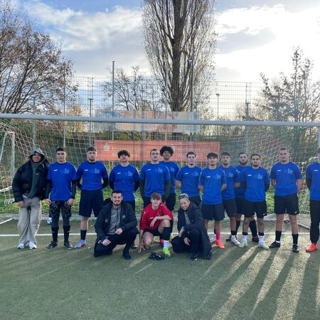 Eine Fußballmannschaft in blauen Trikots posiert auf einem Spielfeld vor einem Tor an einem klaren Herbsttag.