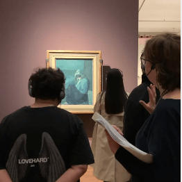 Menschen betrachten ein Gemälde in der Staatsgalerie, während eine Frau mit Notizen darüber spricht.