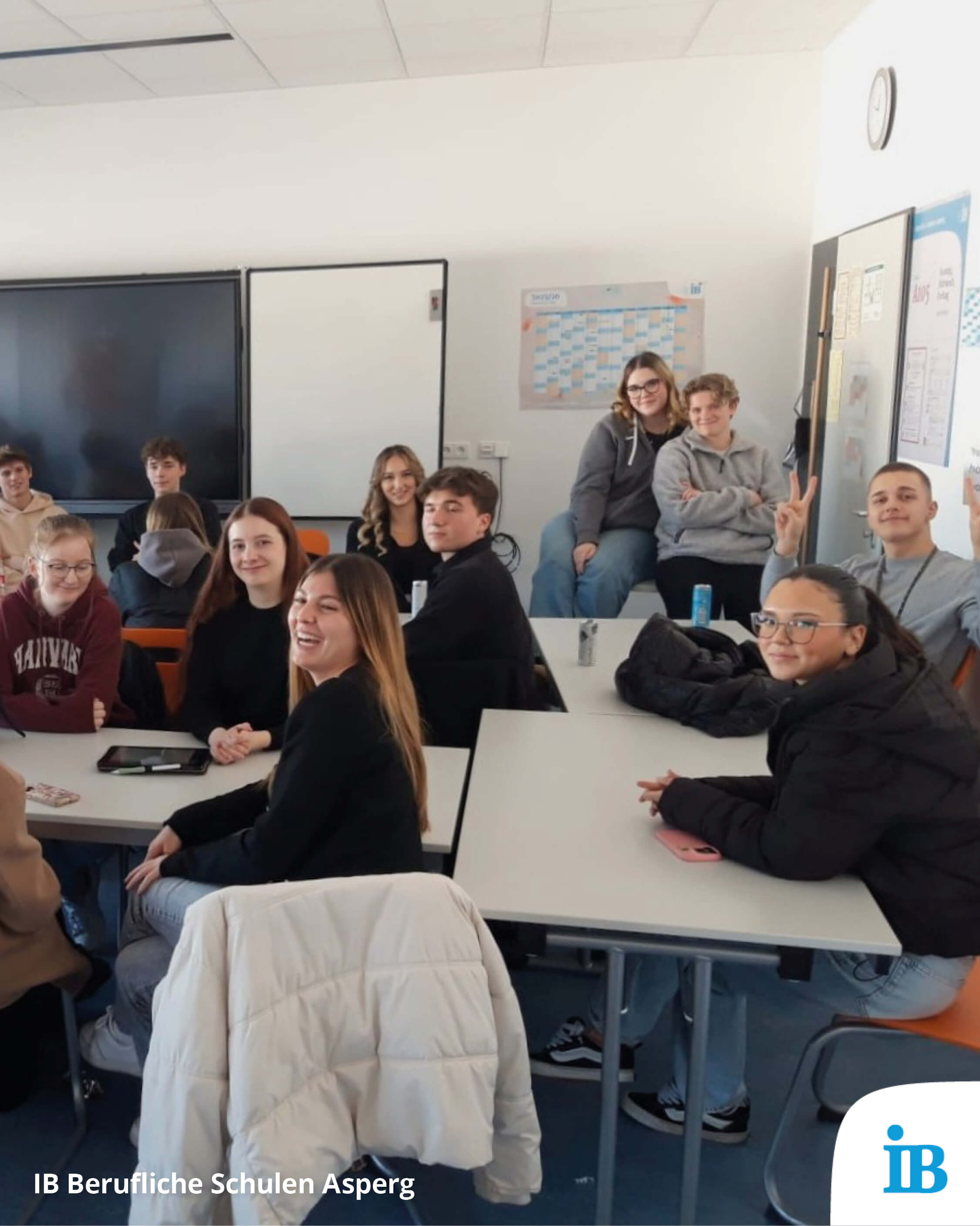 Eine Gruppe von Schülern sitzt in einem Klassenraum zusammen und lächelt fröhlich in die Kamera.