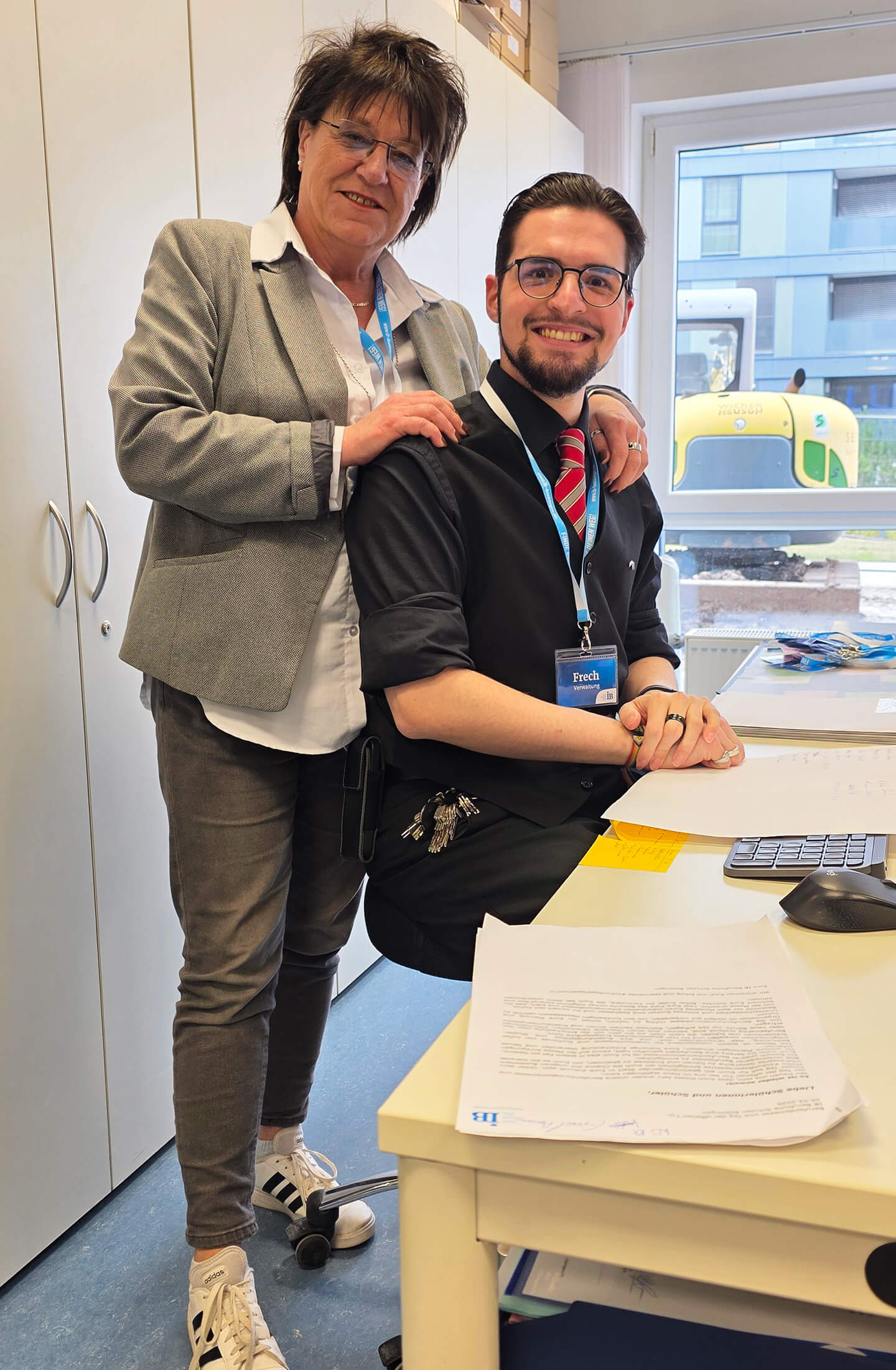 Ein freundliches Schulteam in Böblingen posiert lächelnd am Schreibtisch, während Dokumente und ein Rechner sichtbar sind.