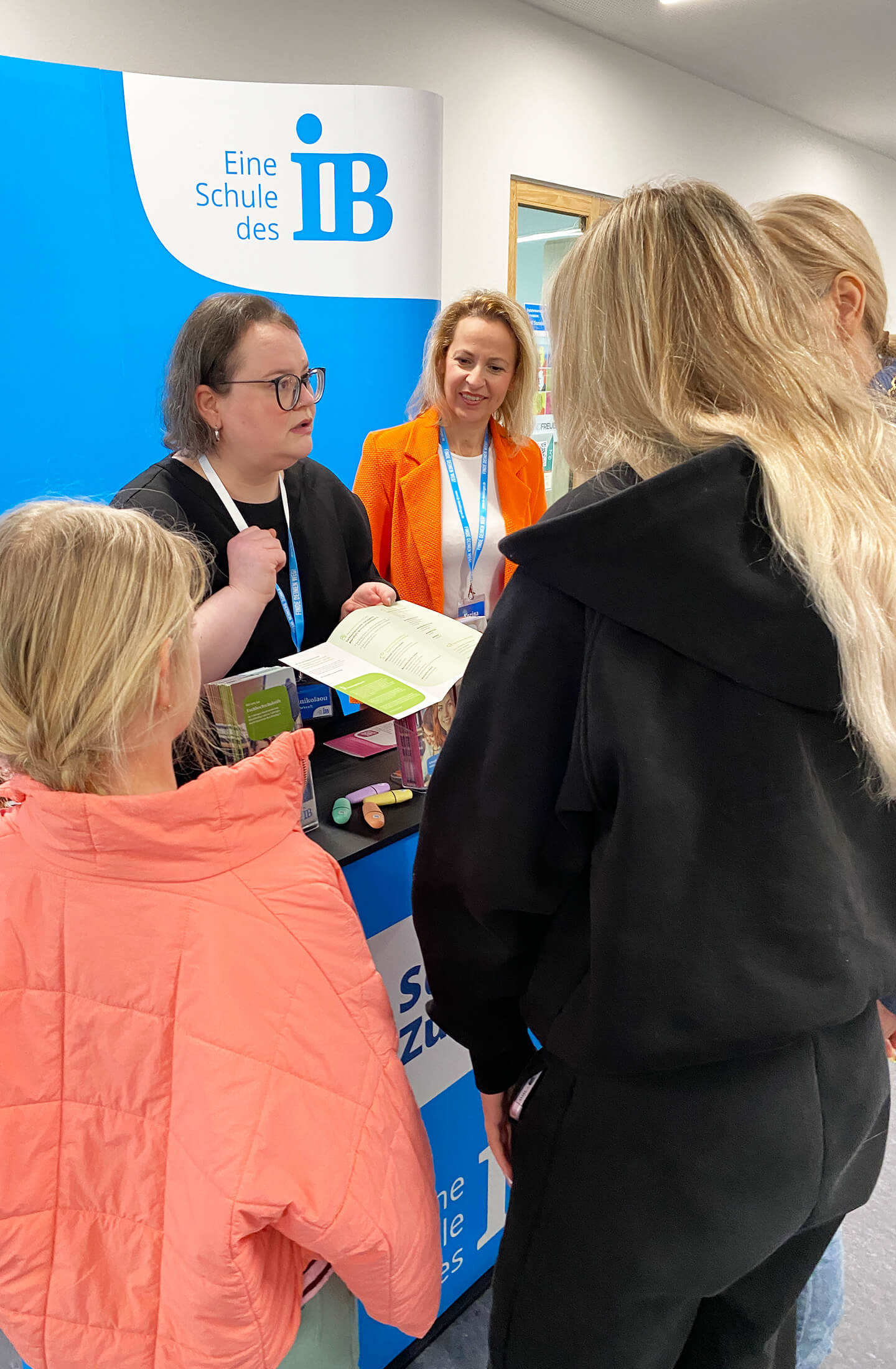 Eine Mitarbeiterin der IB-Schule informiert interessierte Besucher am Stand über Angebote und Programme.
