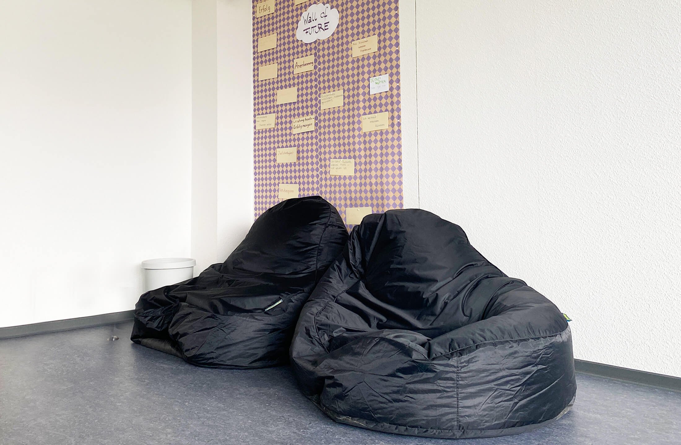 Bequeme schwarze Sitzsäcke stehen in einem modernen Aufenthaltsraum mit einer bunten Wandgestaltung.