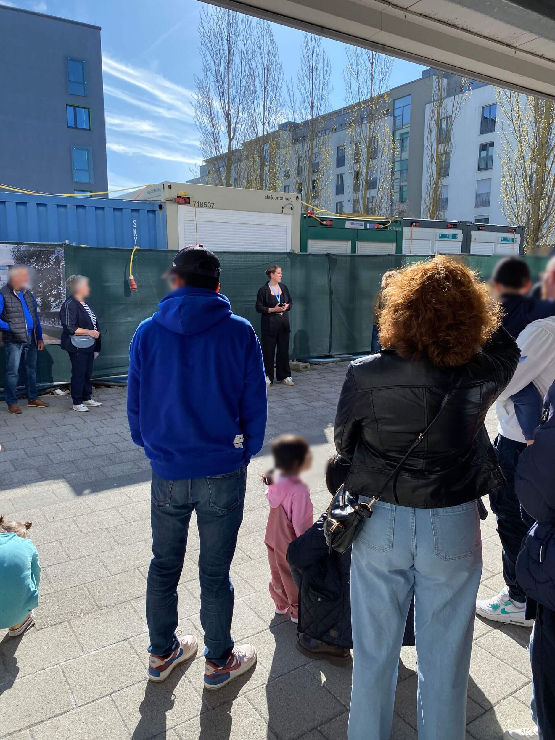 Eine Gruppe von Menschen steht vor einem Bauzaun auf der Baustelle der Grundschule Flugfeld bei der Eröffnung.
