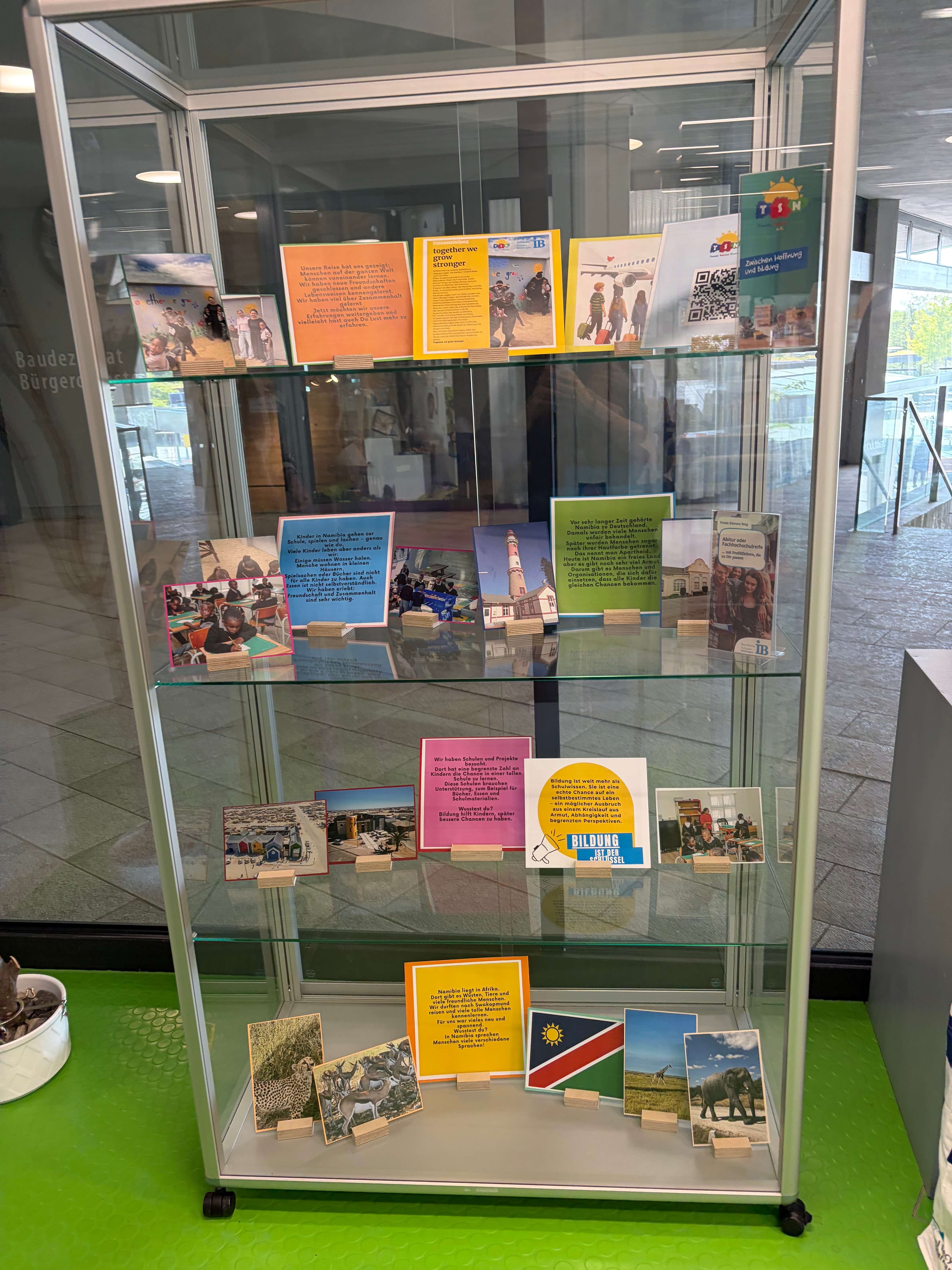 Eine Vitrine zeigt zahlreiche Informationskarten und Fotos zu Bildungsthemen, darunter Namibia und Gemeinschaftsprojekte.
