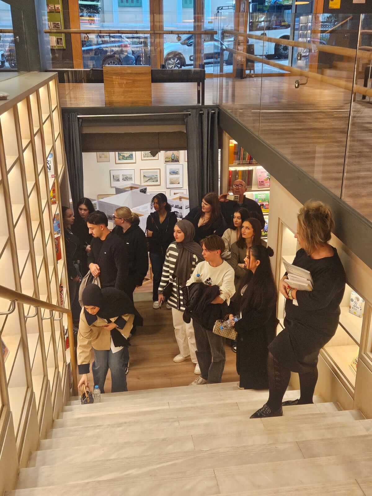 Eine Gruppe Menschen steht auf einer Treppe in einer Galerie, während eine Person sich bückt, um etwas aufzuheben.