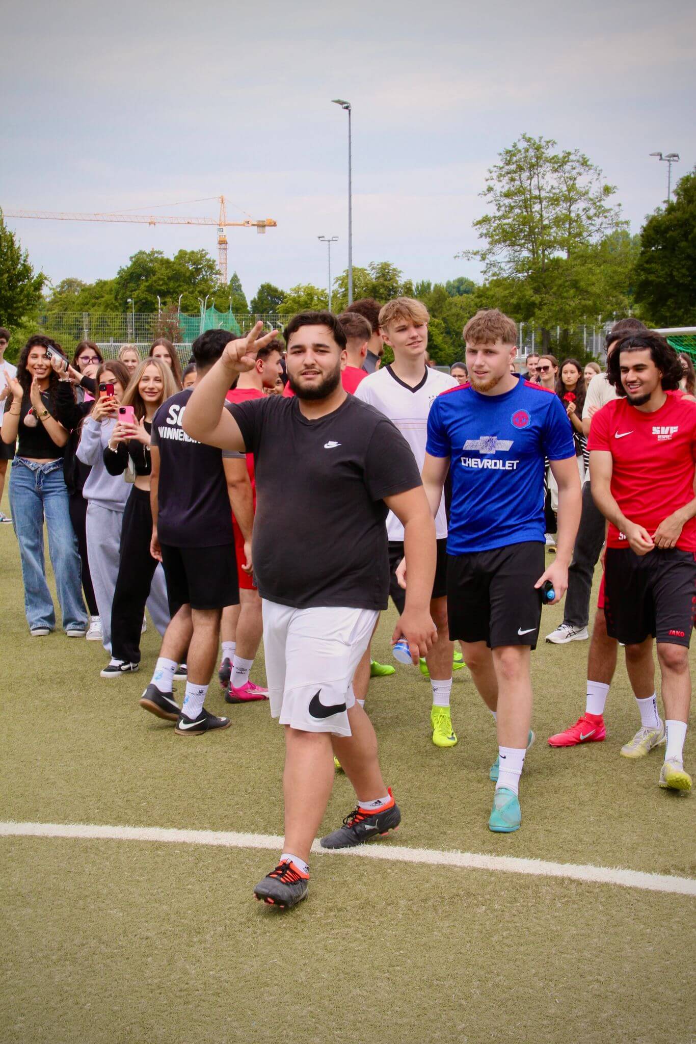 Eine Gruppe junger Männer geht über ein Sportfeld, während Zuschauer am Rand des Rasens stehen und zuschauen.