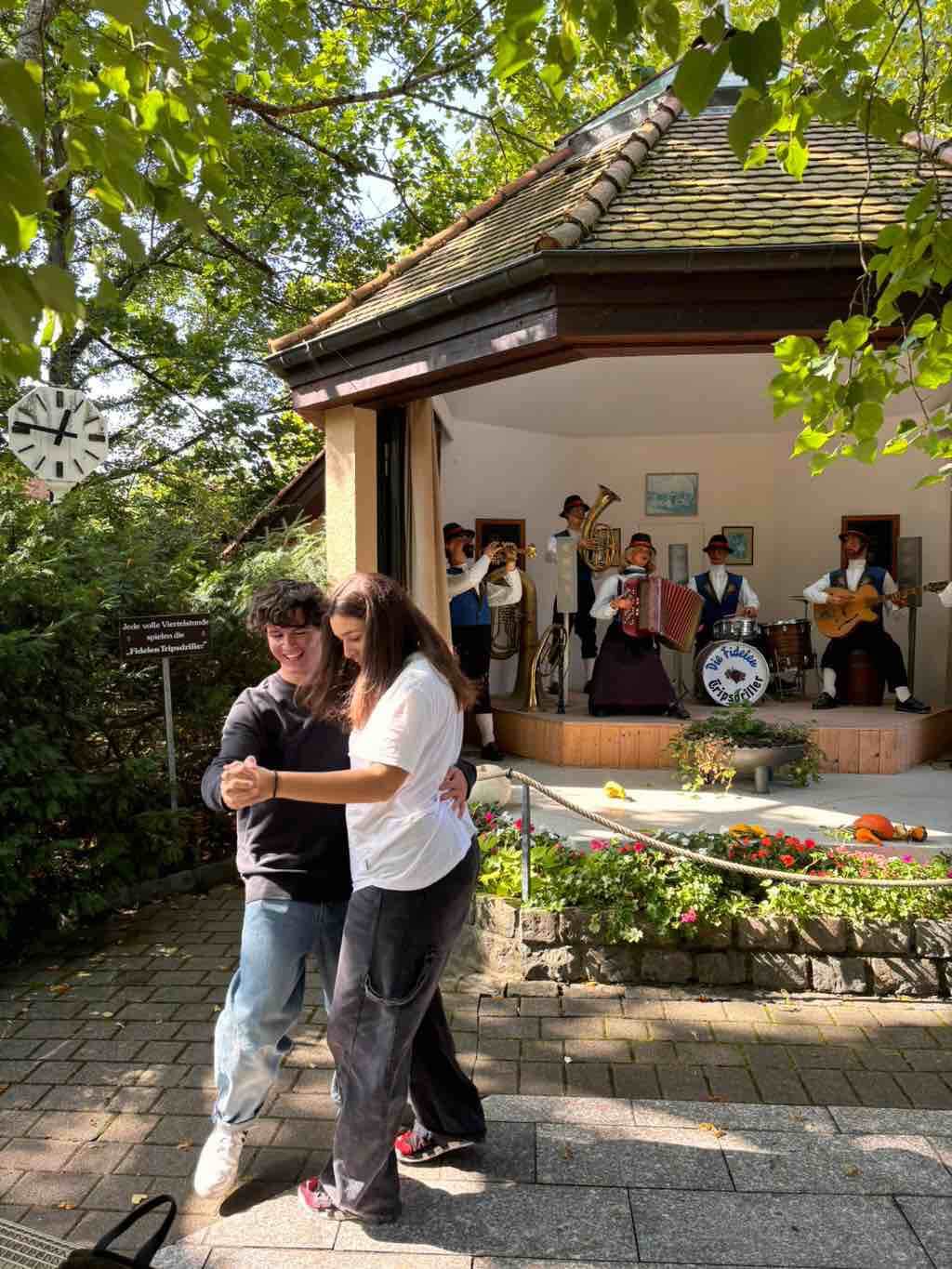 Ein Paar tanzt fröhlich vor einer traditionellen Blaskapelle in einem Pavillon im Freien.