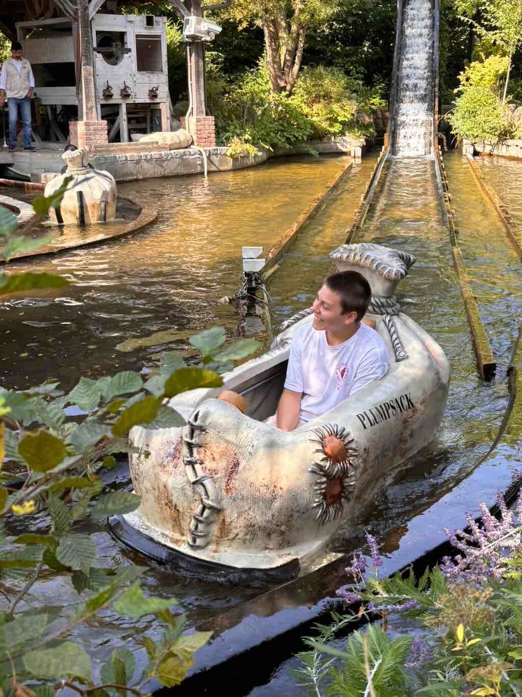 Ein Junge genießt eine Fahrt in einem Boot namens "Plumpsack" auf einer Wasserbahn im Freizeitpark.