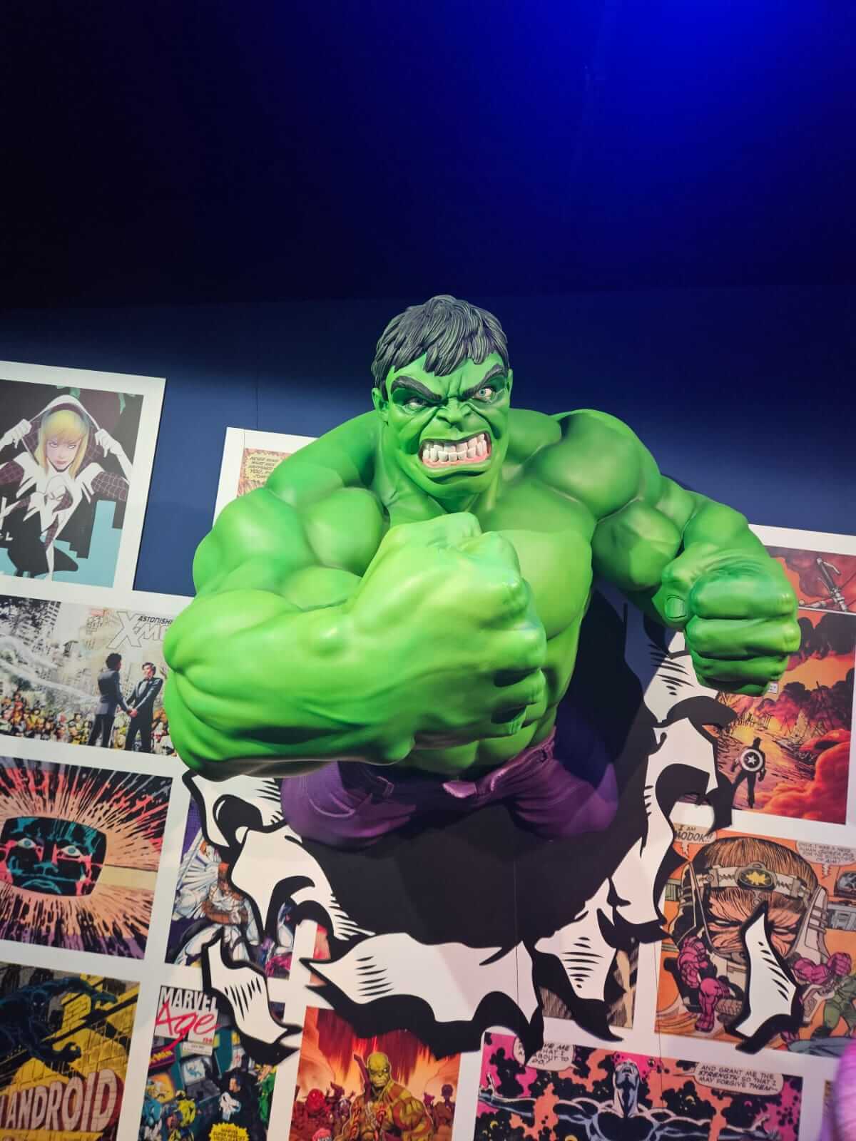 Eine große grüne Figur durchbricht eine Wand aus Comicseiten und wirkt dabei kraftvoll und dynamisch.